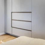 Custom bedroom wardrobe with integrated drawers, white cabinetry, and timber detailing in a modern minimalist bedroom.